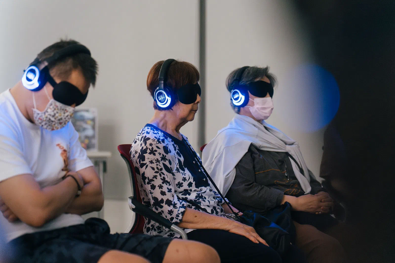 Three participants sit in a row wearing eye masks and illuminated headphones.