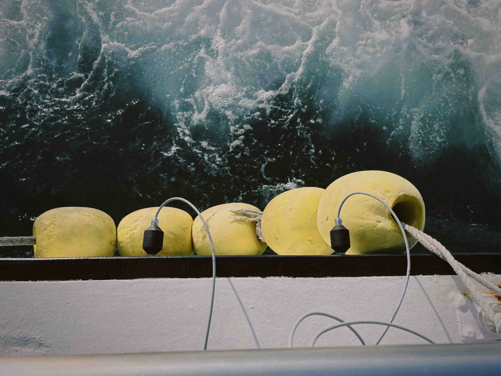 Yellow floats along the edge of a boat, with two black sensors on grey cables, above churning dark water.