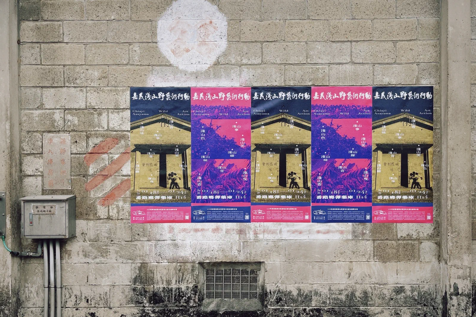 Five colourful posters for the Chiayi Asayama Wild Art Action exhibition pasted in a row on a weathered brick wall.